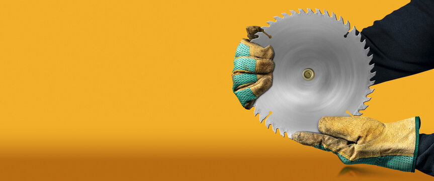 Carpenter with protective work gloves holding a metal circular saw blade, on orange and yellow background with copy space and reflections.