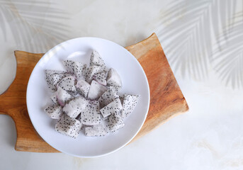 Top view of fresh dragon fruit in white plate with cutting board on marble tabletop decoration