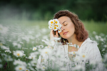 Young beautiful woman enjoying flowers in beautiful chamomile field.