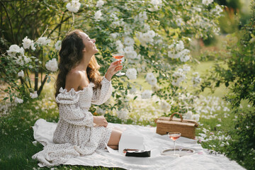 Young beautiful woman with long curly hair having picnic with champagne and fresh eclairs in...