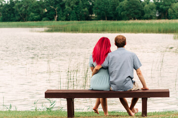 Scene from behind of couple spend time together, relaxing at the park near the lake in the afternoon summer. Back view