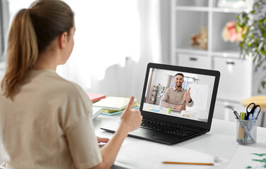 school, education and distance learning concept - female student with teacher on laptop computer screen having video call or online class at home and showing thumbs up