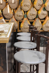 Group of Whole Raw Hams hung on a Wall and a Table and Chairs for Degustation
