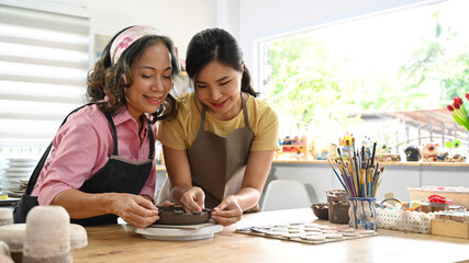 Joyful mature woman making ceramic pot from clay in pottery workshop