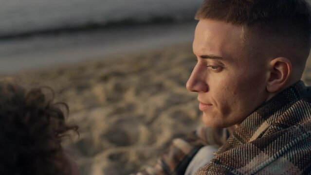 Closeup young couple sitting on sandy beach. Man looking at woman with love