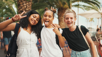 Three girls friends pre-teenage standing on the street smiling, hugging each other making faces for the camera. Three teenagers on the outdoors in urban cityscape background