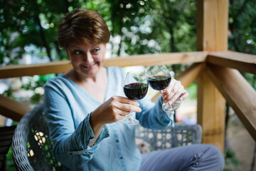 sweet happy middle-aged European woman drinking wine from two glass with same ourside summer, sharing remote drink