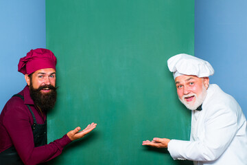 Chef men in cook hat pointing spoon on blank board menu. Chef, cook or baker by empty chalkboard menu.