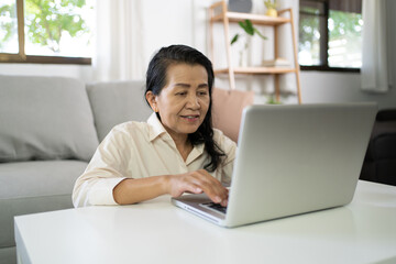 Middle age Asian woman Work from home. senior woman smiling Beautiful mature asian woman on laptop with technology concept