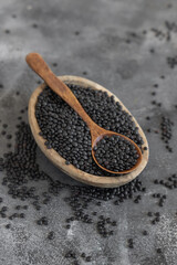 Bowl of dry black lentils beans with a spoon on grey table close up, protein source for vegetarian diet