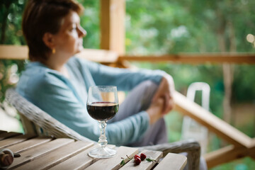 sad middle-aged European woman drinking wine from glass outside summer, alone and looking away