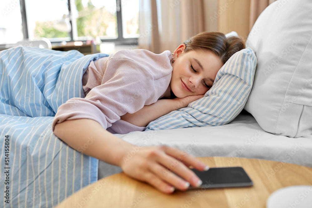 Wall mural people, bedtime and rest concept - happy smiling teenage girl with smartphone lying in bed at home