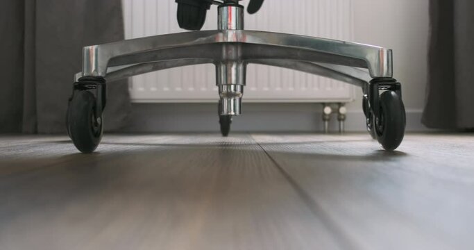 Office chair rolls over on camera. Close-up on the wheels of the chair, silently rolling on the floor surface.