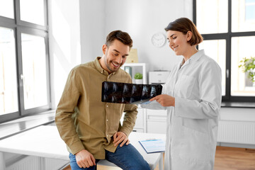 medicine, healthcare and people concept - happy smiling female doctor showing x-ray to male patient...