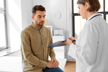 Fototapeta premium medicine, healthcare and people concept - female doctor showing clipboard to man patient at hospital