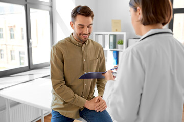 Obraz premium medicine, healthcare and people concept - female doctor showing clipboard to smiling man patient at hospital