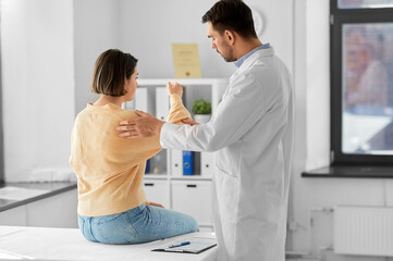 Fototapeta premium medicine, healthcare and people concept - male doctor with clipboard talking to woman showing her sore arm patient at hospital