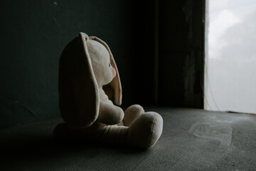 Lost toy bunny is sitting alone in a room. War, death and lost childhood concept - obrazy, fototapety, plakaty