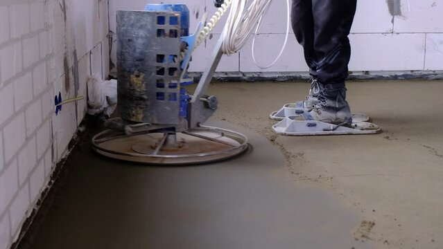Ramming and grinding of semi-dry floor screed by a machine with a rotating disk for leveling. Construction of a concrete floor in the house, a master with special equipment. Slow motion