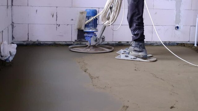 Ramming and grinding of semi-dry floor screed by a machine with a rotating disk for leveling. Construction of a concrete floor in the house, a master with special equipment. Slow motion