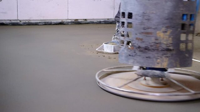 Ramming and grinding of semi-dry floor screed by a machine with a rotating disk for leveling. Construction of a concrete floor in the house, a master with special equipment. Slow motion