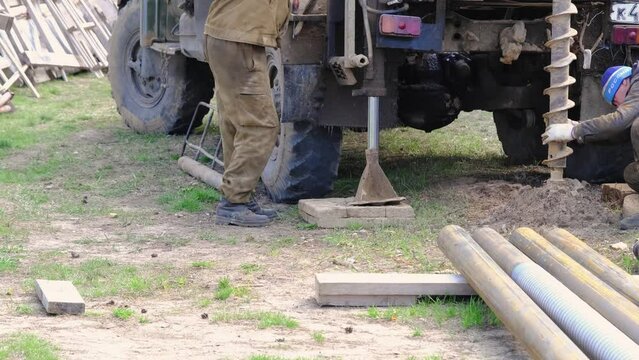 Team of workers with drilling rig on car are drilling artesian well for water in ground. Insertion of metal casing pipe into ground, installation of individual drinking supply, June 28, 2022, Russia, 