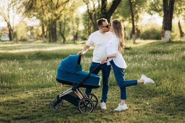 A young family walk in the park in  with a toddler in a stroller. Happy parents