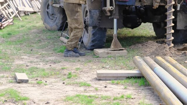 Team of workers with drilling rig on car are drilling artesian well for water in ground. Insertion of metal casing pipe into ground, installation of individual drinking supply, June 28, 2022, Russia, 