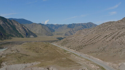 Traffic cars on road between mountains of Altai under clear blue sky