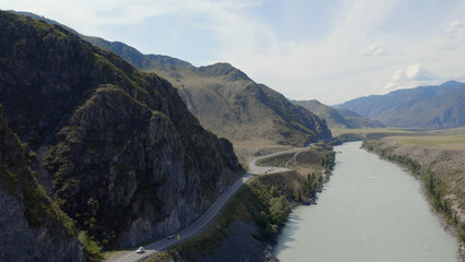 Traffic cars on Chuya highway road between mountains and Katun river under blue sky in Altai