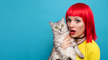 A young beautiful girl with a cat in her arms, isolated on a blue background. Expressive and funny...