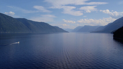 Boats on lake Teletskoye between mountains with blue clear sky in Altai