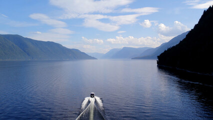 Motorboat on lake Teletskoye between mountains with blue clear sky in Altai