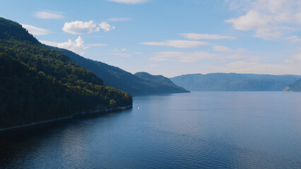 Boats on lake Teletskoye between mountains with blue clear sky in Altai