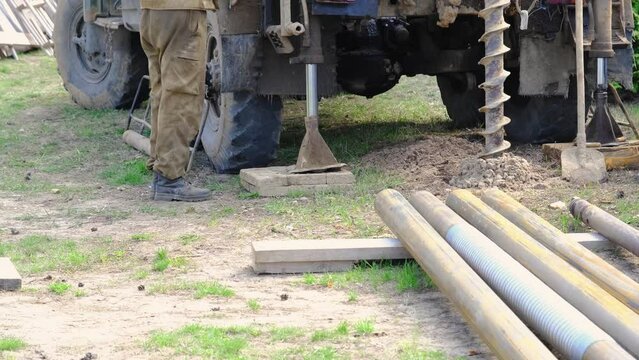 Team of workers with drilling rig on car are drilling artesian well for water in ground. Insertion of metal casing pipe into ground, installation of individual drinking supply, June 28, 2022, Russia, 