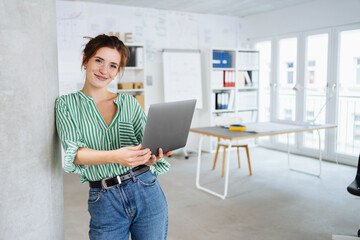 Young business woman standing with laptop in office - 514169636