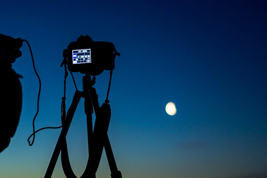 Black camera on tripod is taking a moon photo