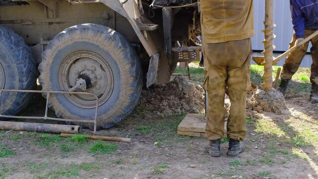 Team of workers with drilling rig on car are drilling artesian well for water in ground. Insertion of metal casing pipe into ground, installation of individual drinking supply, June 28, 2022, Russia, 