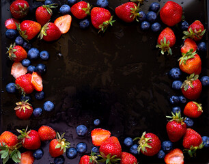 Strawberries and blueberries on a black background with water drops. Summer background with berries