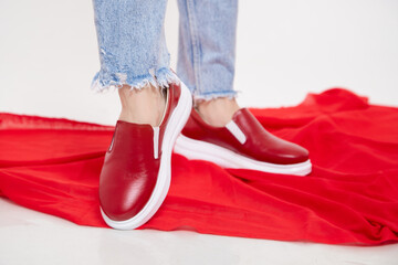 Red beautiful fashionable female loafers shoes on leg of girl or woman. Studio shoot on white...
