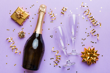 Bottle of champagne with colored glitter, confetti and gift box space for text on colorfull background, top view. Hilarious, christmas and birthday celebration