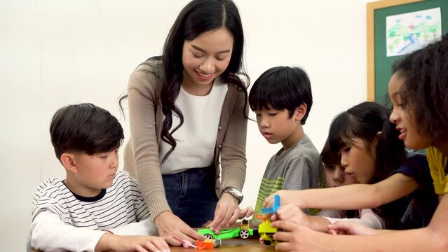 Young woman working in school helping multiethnic children make toy cars, learning about mechanics, stem. Asian school teacher assisting elementary students in science classroom