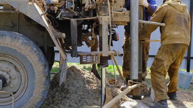 Team of workers with drilling rig on car are drilling artesian well for water in ground. Insertion of metal casing pipe into ground, installation of individual drinking supply, June 28, 2022, Russia, 