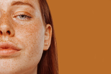 Close-up portrait of half face red-haired girl with freckle and blue eye. Beautiful young woman's...
