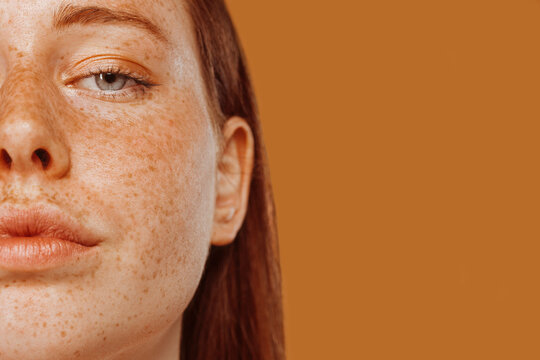Close-up portrait of half face red-haired girl with freckle and blue eye. Beautiful young woman's face shot. Female model with perfect skincare, human emotions, facial expression, beauty and cosmetics