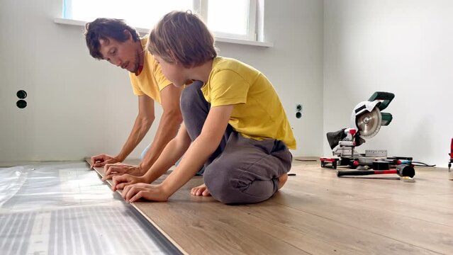 Father and his little son install laminate on the floor in their apartment. DIY concept. Slowmotion video