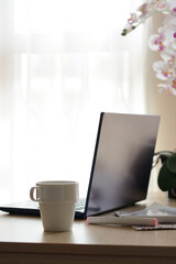 Fototapeta premium Ceramic cup, laptop and stationery on wooden table indoors. Good morning