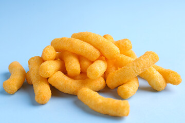 Heap of tasty cheesy corn puffs on light blue background, closeup view