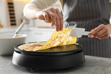 Woman cooking delicious crepe on electric pancake maker in kitchen, closeup - obrazy, fototapety, plakaty