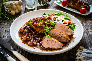 Roasted pork loin with shimeji mushrooms in sauce, fresh thyme, greens and cherry tomatoes on...
